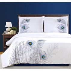 a white bed with blue and green feathers on it's comforter in a bedroom