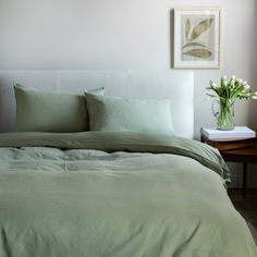 a bed with green sheets and pillows in a bedroom next to a table with flowers on it