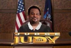 judge judy sitting at his desk with an american flag in the background