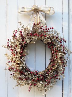 a wreath hanging on the side of a white door with red berries and gold leaves