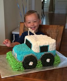 a young boy sitting in front of a cake shaped like a tractor with grass on it