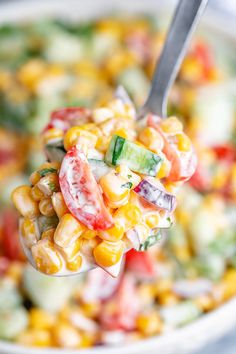 a spoon full of corn salad with cucumbers and tomatoes