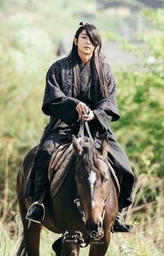 a woman riding on the back of a brown horse in a field with tall grass