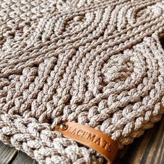 a close up of a knitted blanket on a wooden surface with a leather tag