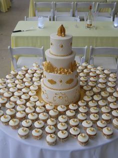 a table topped with lots of cupcakes and a white cake covered in gold frosting