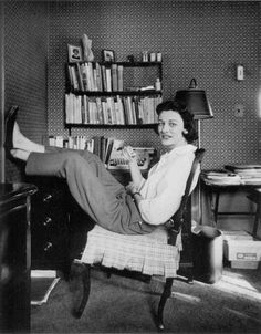 an old photo of a woman sitting in a chair with her feet on the desk