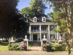 a large white house sitting next to a lush green park filled with trees and flowers