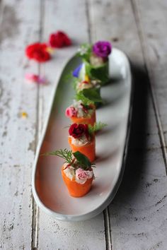 small appetizers are lined up on a long white platter with flowers in them