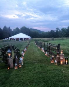 candles are lit in front of a wooden fence on a grassy field with a white tent behind it