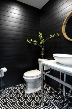 a white toilet sitting next to a sink in a bathroom under a round mirror on a black wall