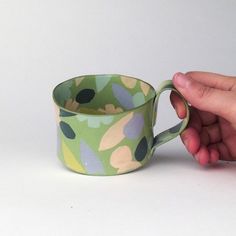 a hand holding a green and pink coffee cup on top of a white countertop