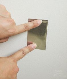 a person is holding a square piece of tin foil in their left hand and pointing to it on the wall