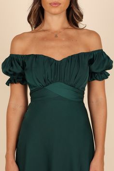 a woman wearing a green dress with ruffles on the shoulders and shoulderline