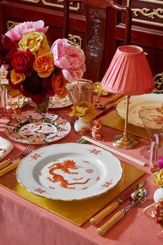 the table is set with pink and orange flowers in vases, plates, silverware, napkins, and gold cutlery