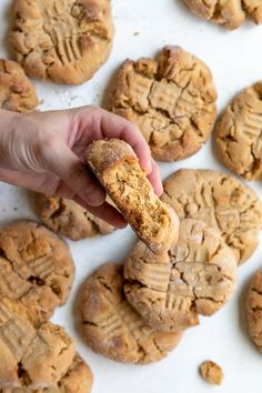 a hand holding a cookie in front of a group of cookies on a white surface