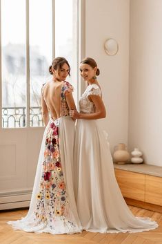 two women standing next to each other in front of a window wearing dresses with flowers on them