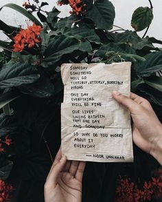 someone holding up a piece of paper with writing on it in front of some flowers