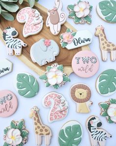 various decorated cookies on a wooden tray with leaves and flowers in the background, including giraffes