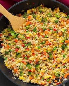 a skillet filled with rice and vegetables on top of a red cloth next to a wooden spoon