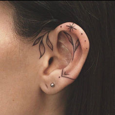 a woman's ear with an arrow and stars tattoo on her left behind the ear