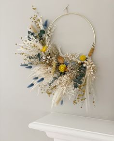 a wreath made out of dried flowers and feathers hanging on a white wall above a fireplace mantel