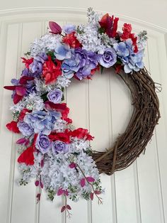 a wreath with purple, red and white flowers hanging on the front door for decoration