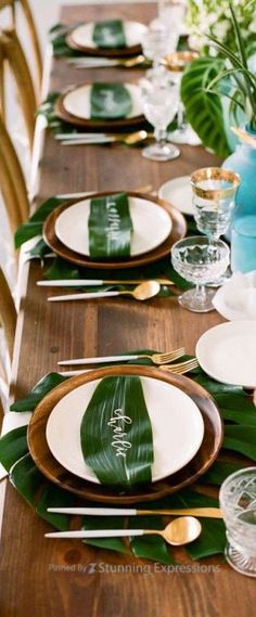 the table is set with plates, silverware and green leafy napkins on it