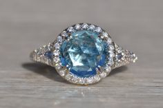 an oval shaped blue diamond ring with halos around the band on a wooden surface