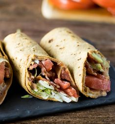 two burritos with meat, lettuce and tomato on a black plate