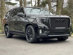 the front end of a black gmc suv parked in a parking lot next to trees