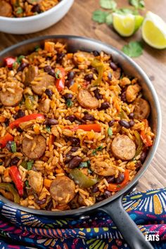 a skillet filled with rice, sausage and beans on top of a wooden table