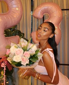 a woman holding a bouquet of flowers in front of pink balloons and number 3 decorations