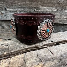 "Brown leather bracelet that has a paisley filigree. It is adorned with antique silver and copper flower pattern with turquoise center western conchos (W220). Measures 7.75\" to 8.25\" with two snaps to create two sizes." Brown Bohemian Leather Bracelet With Concho, Rustic Brown Bracelet With Concho, Rustic Brown Concho Bracelets, Southwestern Style Brown Concho Bracelets, Rustic Brown Cuff Bracelet With Concho, Brown Hand Tooled Jewelry For Rodeo, Hand Tooled Brown Jewelry For Rodeo, Vintage Concho Leather Bracelet For Festival, Vintage Leather Concho Bracelet For Festival