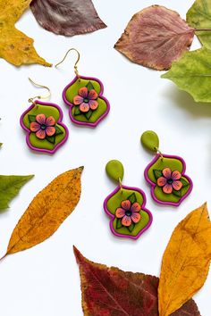 two pairs of earrings with flowers on them sitting next to leaves and fall colors in the background