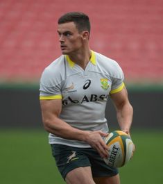 a man holding a rugby ball on top of a field