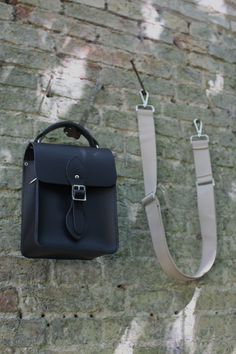 lifestyle image of black leather mini crossbody mens and womens bag with interchangeable straps - The Binocular Bag in Black Celtic Grain and Sand Webbing Strap from The Cambridge Satchel Co.