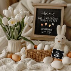 a white bunny sitting on top of a bed next to an egg basket and flowers