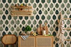 a kitchen with green leaf wallpaper and wooden shelves on the wall, next to a wicker sideboard