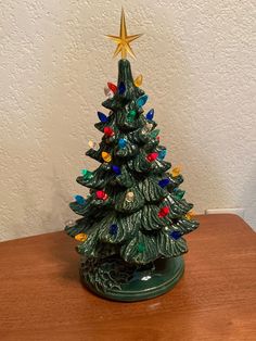 a small christmas tree with lights on it sitting on a wooden table next to a white wall