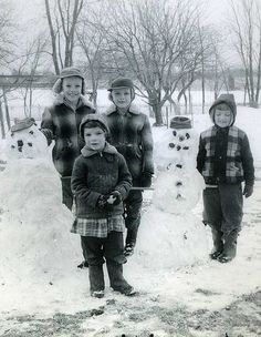 three children standing in front of a snowman with two adults and one child looking at the camera