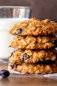 three blueberry oatmeal cookies stacked on top of each other next to a glass of milk