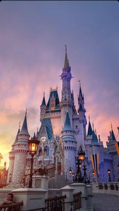 the castle is lit up at night in front of an orange and pink sky with clouds