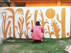 a woman painting a mural on the side of a building with orange and white designs