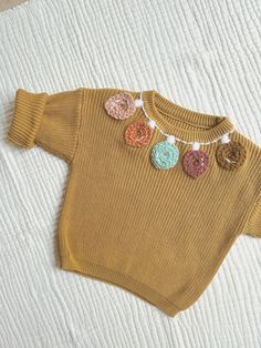 a brown sweater with crocheted flowers on the collar and sleeves is laying on a bed