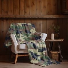 a camo print blanket sitting on top of a white chair next to a wooden wall