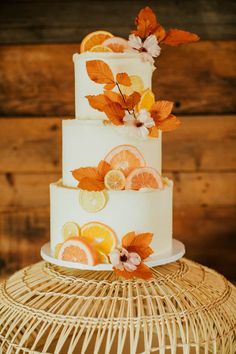 a three tiered cake with oranges and leaves on it sitting on a wicker stand