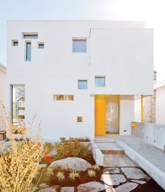 a white house with yellow doors and steps leading to the front door is surrounded by plants