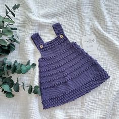 a purple crocheted dress sitting on top of a bed next to a plant