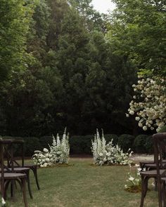 chairs and tables in the middle of a grassy area with flowers on each side, surrounded by trees