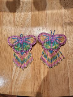 two butterfly shaped beaded earrings sitting on top of a wooden table